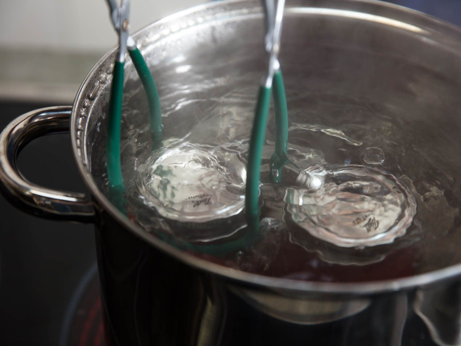 Jars of tomatoes lowered into a pot of boiling water