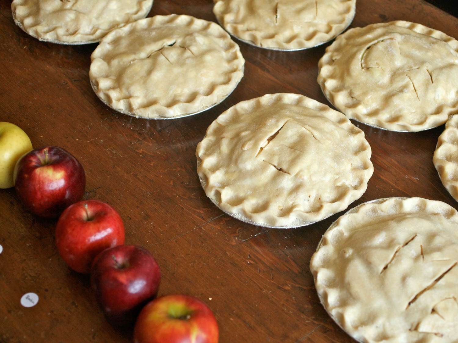 几个未烤的苹果派在木头表面上排列着，旁边是一排苹果
