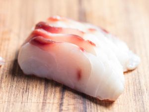 Slices of sushi-grade raw fish on a wooden board.