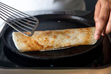 Rolling a cooked dosa on a cast iron griddle