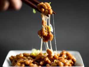 筷子夹着纳豆放在方形盘子上，纳豆是一种发酵的大豆，是日本常见的早餐。