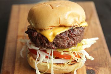 A fully loaded cheese burger to tomatoes and onions on a cutting board