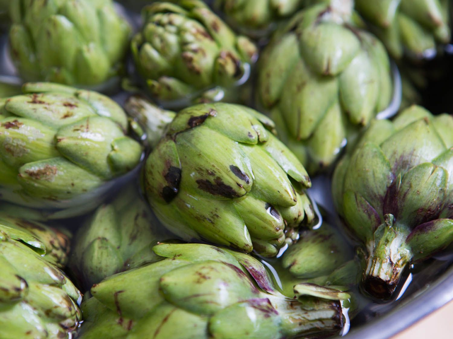 Close-up of many untrimmed artichokes in a metal pan.