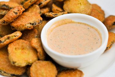A bowl of remoulade sauce next to a pile of sliced fried vegetables.
