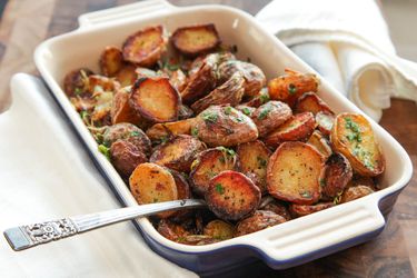 Casserole dish filled with roasted new potatoes with spoon sticking out.