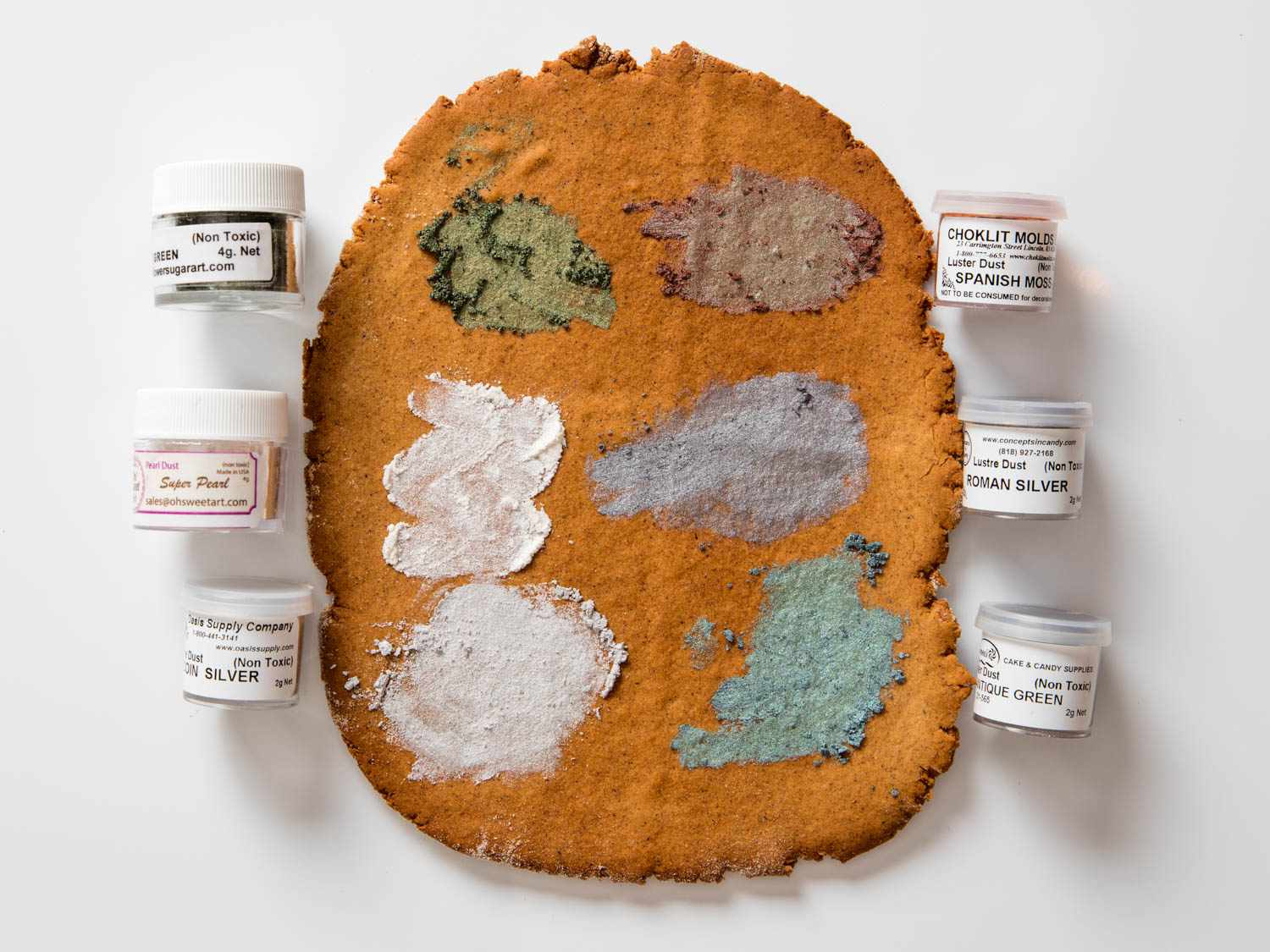 Samples of luster dust in various dull colors, against a slab of gingerbread