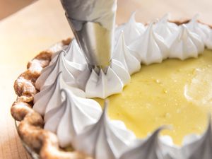 a piping bag piping meringue onto the filling of a fresh and creamy lime pie.