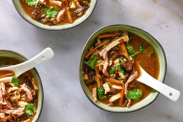 Three bowls of hot and sour soup, each with a ceramic soup spoon in it.