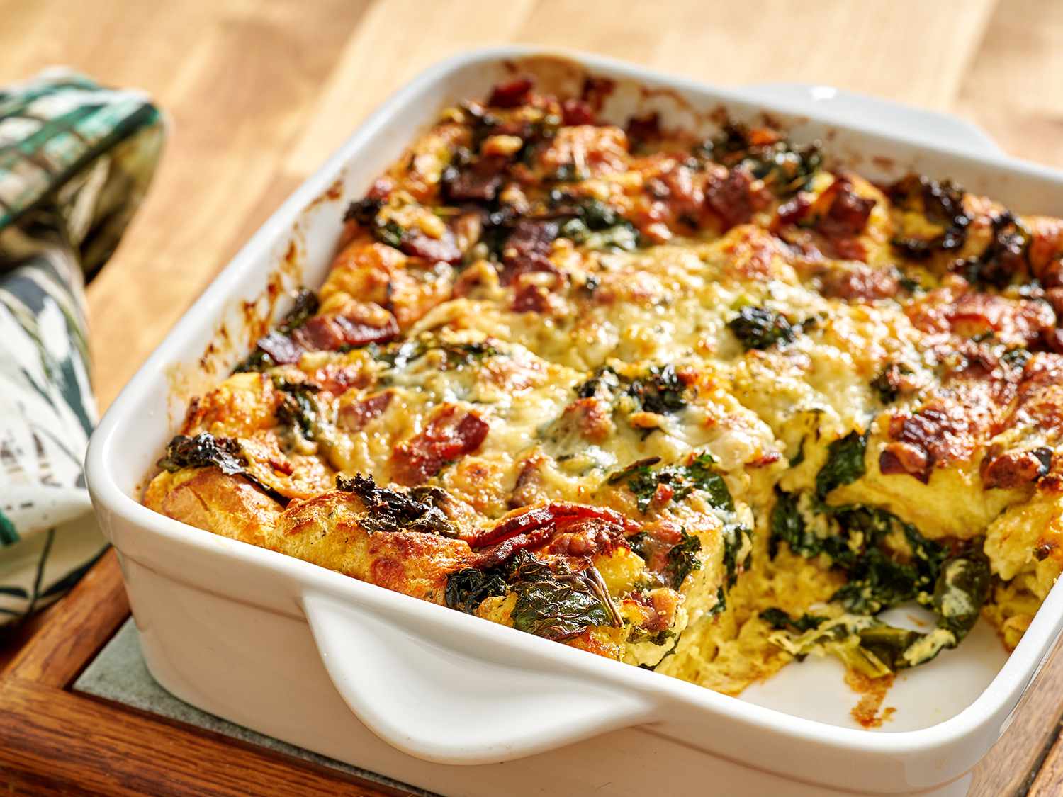 Kale and bacon strata in a baking dish with one portion removed