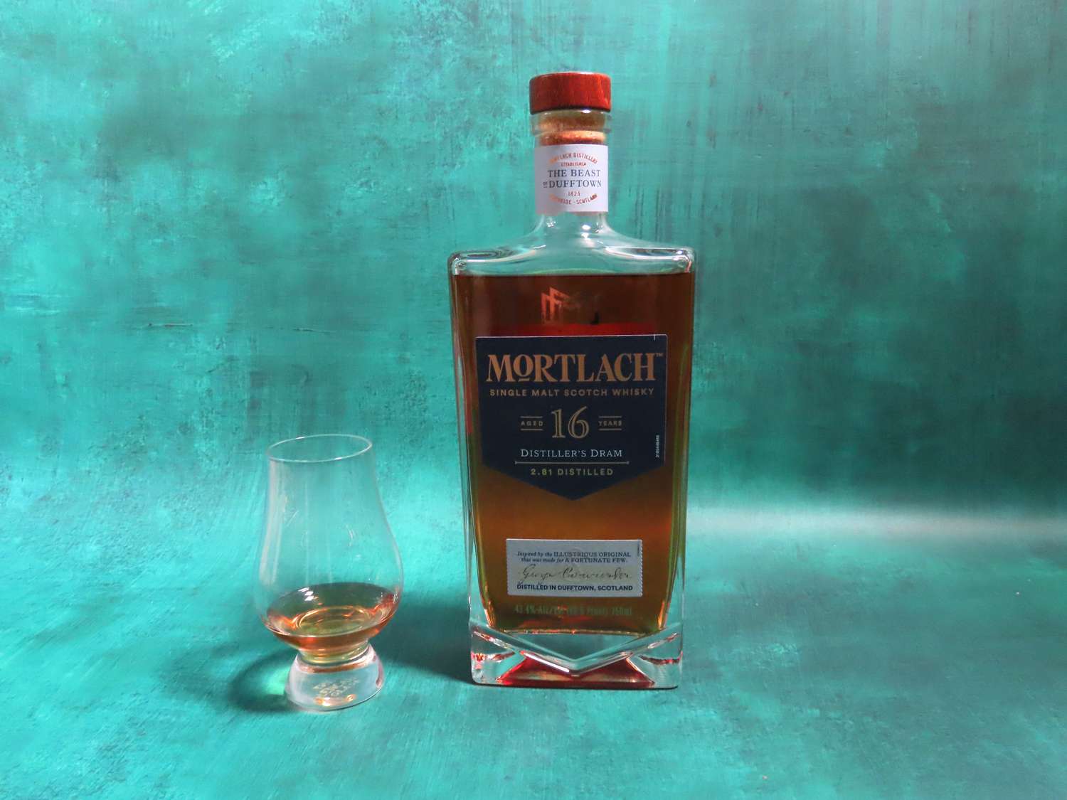 a bottle of mortlach on a blue surface with a whisky glass beside it