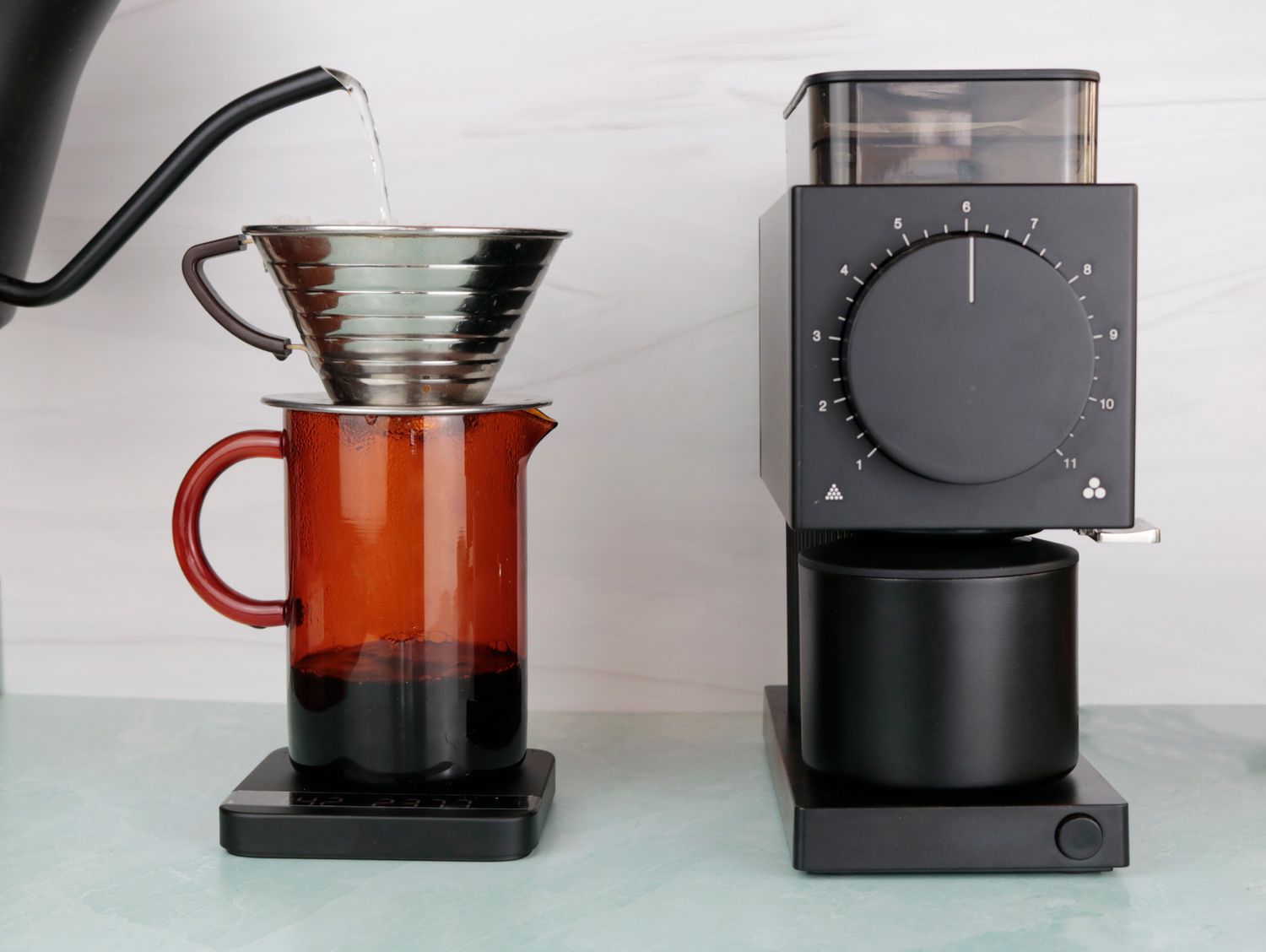 a gooseneck kettle pouring water into a pourover dripper next to a Fellow Ode Gen 2 grinder