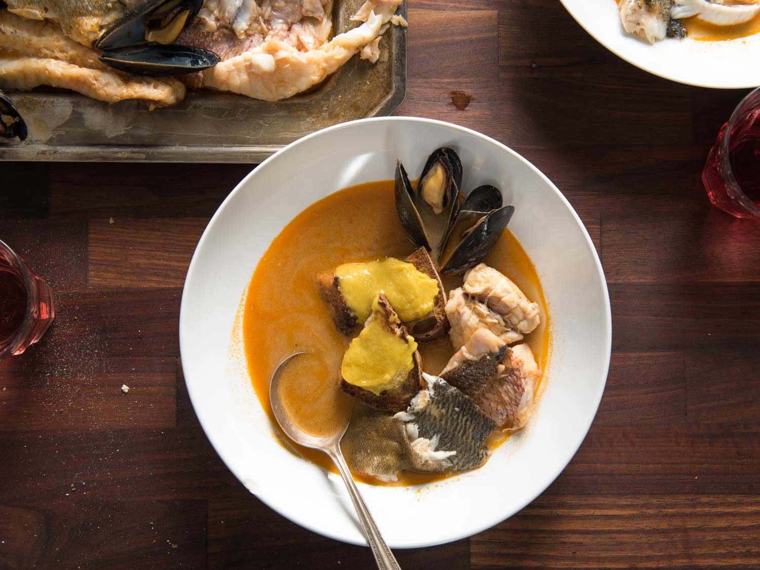 Top down view of a bowl of bouillabaisse, topped with mussels, pieces of fish and rouille.