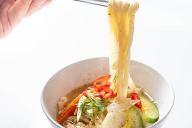 A bowl of Korean knife-cut noodle soup, showing chopsticks lifting noodles from the bowl below.