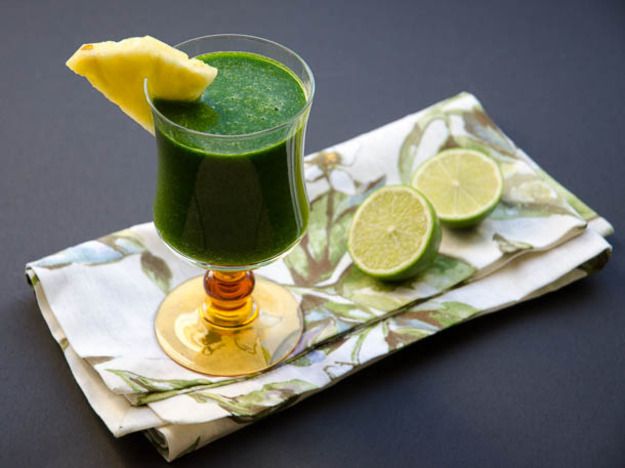 一杯热带绿色果汁放在餐巾上，杯子旁边放半片酸橙，杯沿放一块楔形菠萝。