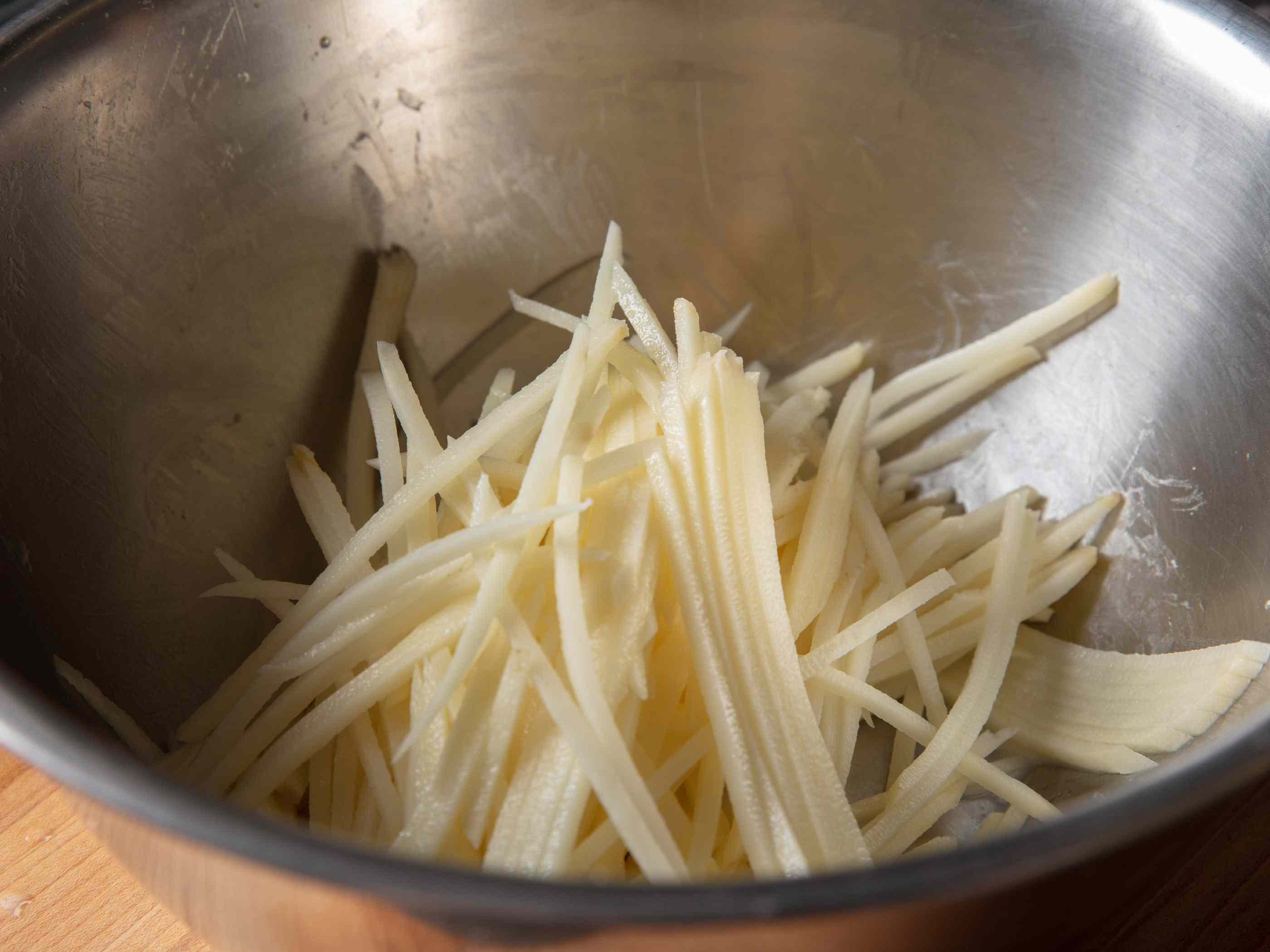 将生土豆丝放入搅拌碗中。