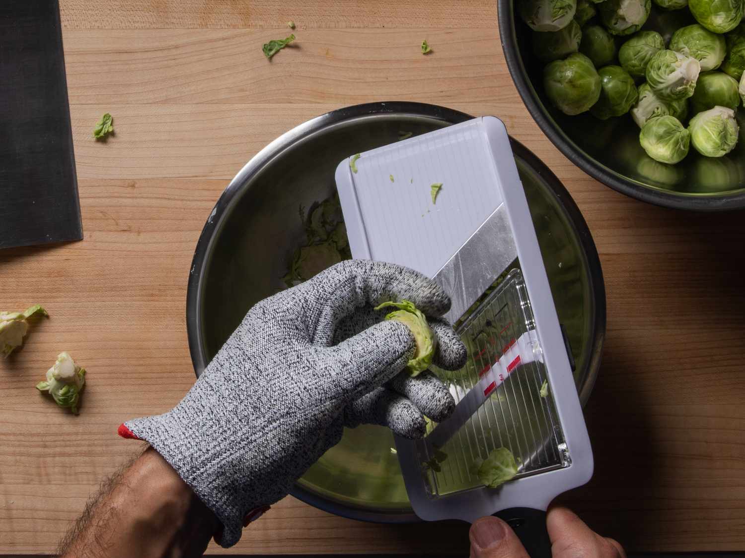 Shaving a Brussels sprout using a mandoline slicer into a bowl below.