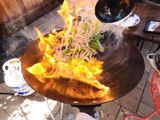 Food being tossed in wok with flames on an outdoor wok burner