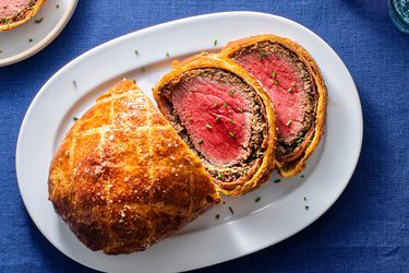 Sliced beef Wellington on a white ceramic plate on a blue linen tablecloth.