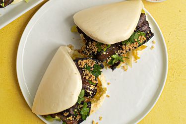 Two Taiwanese pork belly buns (Gua Bao) placed on a white ceramic plate on a yellow background.