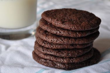 Stack of thin chocolate cookies next to glass of milk