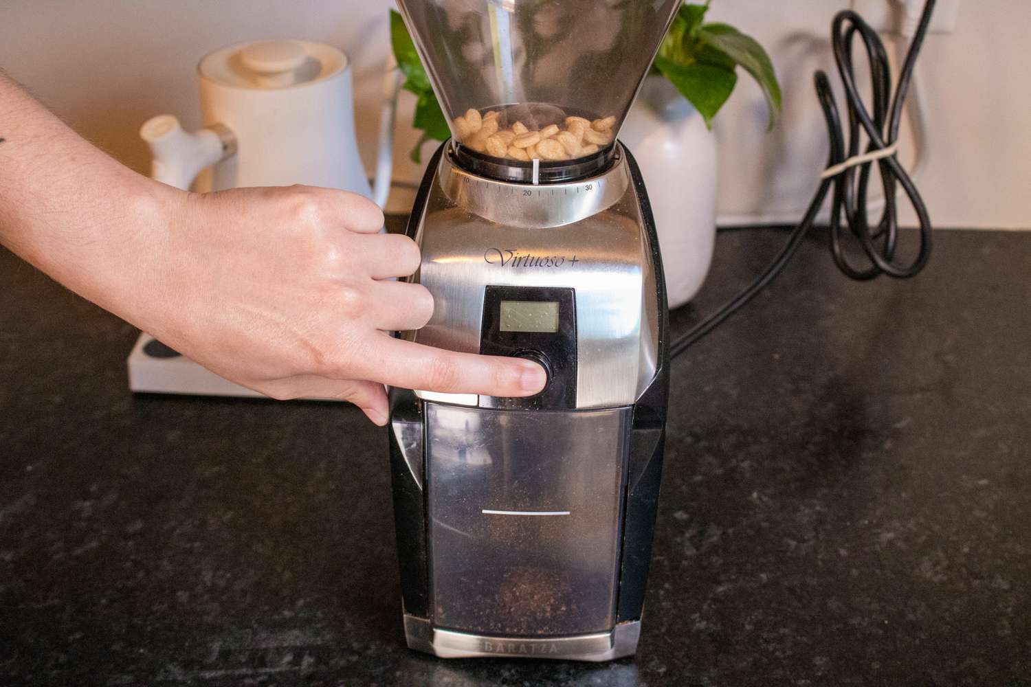 A hand pressing down on the start button a coffee grinder