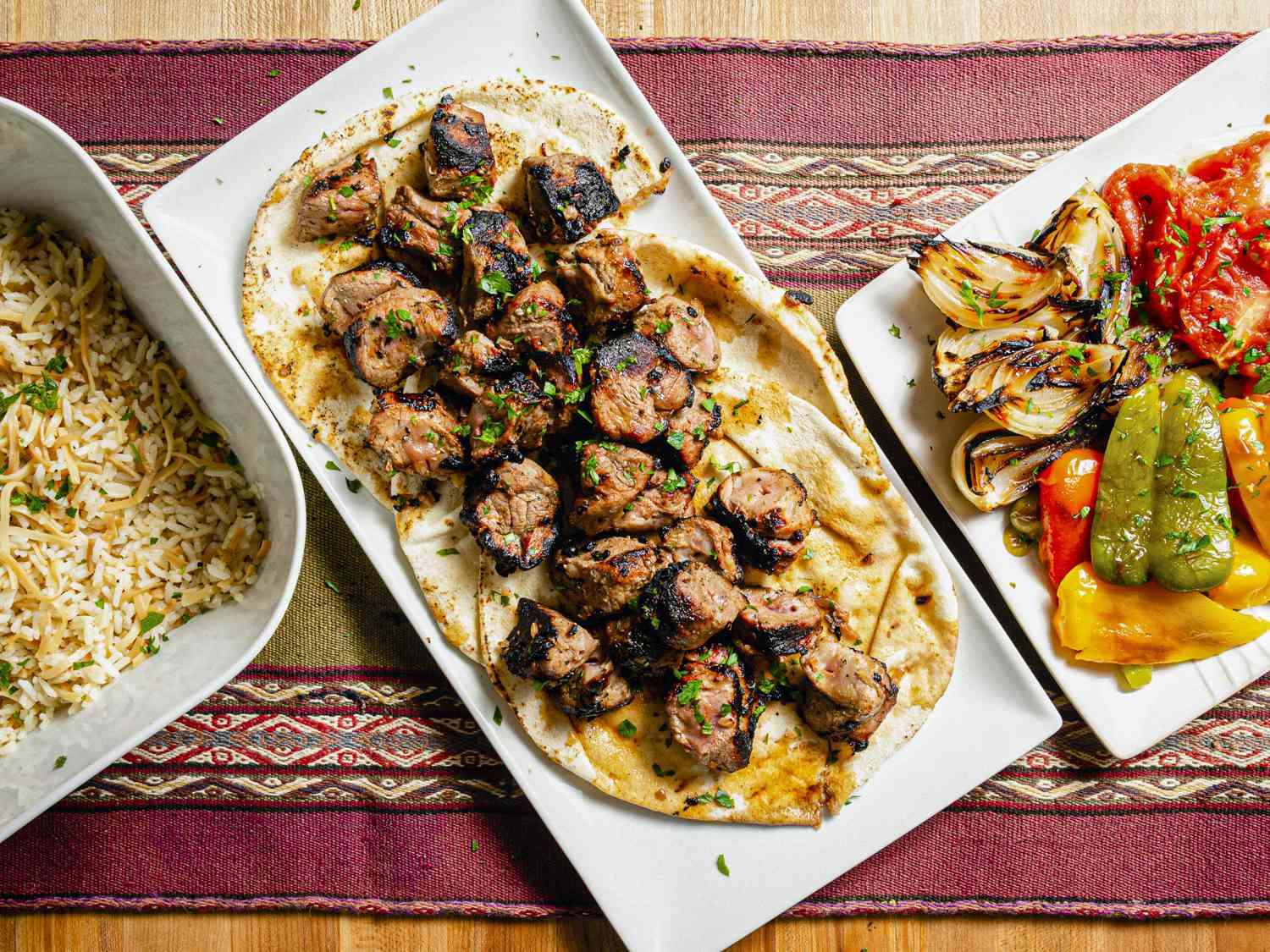 Overhead view of finished shish kebabs on pita with salads and roasted vegetables