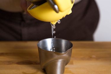 Juice being squeeze from a lemon into a small metal measuring cup.