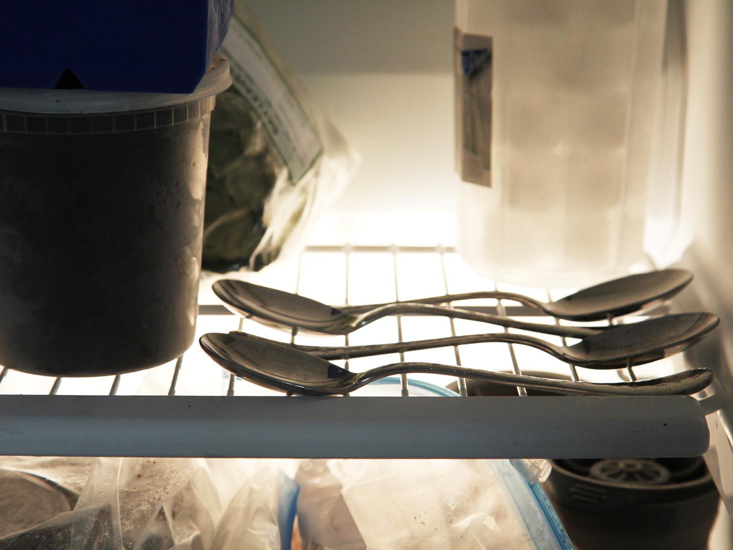 把三个勺子放在冰箱的架子上，旁边放着各种塑料容器和冷冻袋
