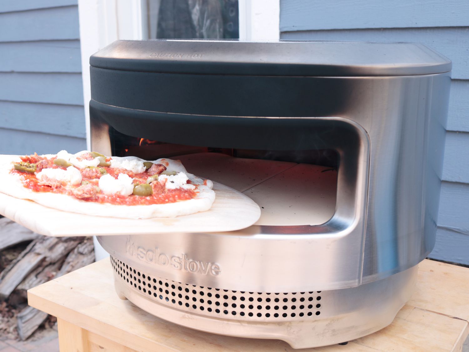 a pizza is launching from a wooden peel into the Solo Stove Pi pizza oven