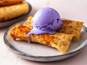 two turon on a plate with a scoop of ube ice cream dripping down the side