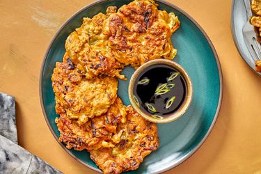 Vegetable pancakes on a blue plate with dipping sauce sprinkled with scallions.