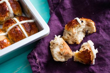 A pulled apart homemade hot cross bun next to the pan of buns.