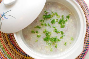 A finished pot of pork and sweet corn congee, garnished with sliced scallions.