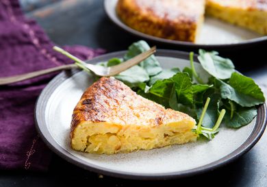 A slice of Spanish potato and onion tortilla on a small grey plate with salad on the side.