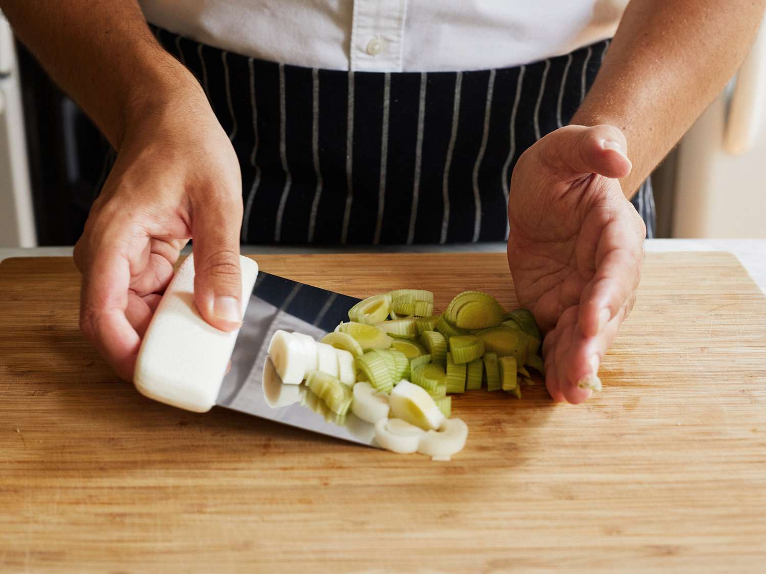 Using a bench scraper to scoop up chopped leek rounds