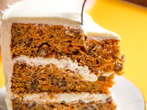 A fork diving into a slice of a 3-layer brown butter carrot cake with cream cheese buttercream frosting.