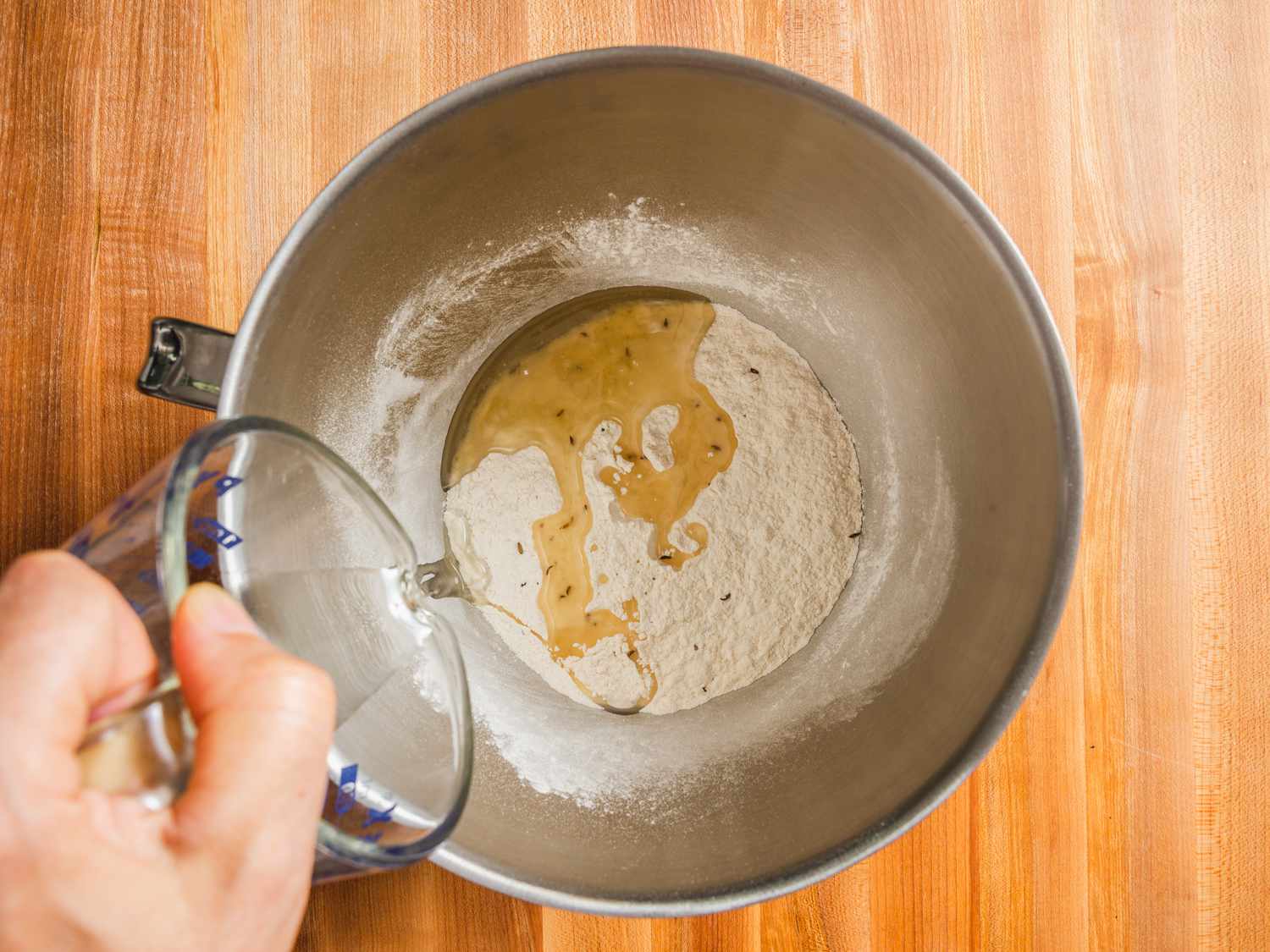 俯视图的干混合萨莫萨面团在一个立式搅拌碗与油从量杯倒进碗