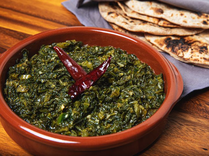 Saag in an earth-toned orange bowl with roti in the background