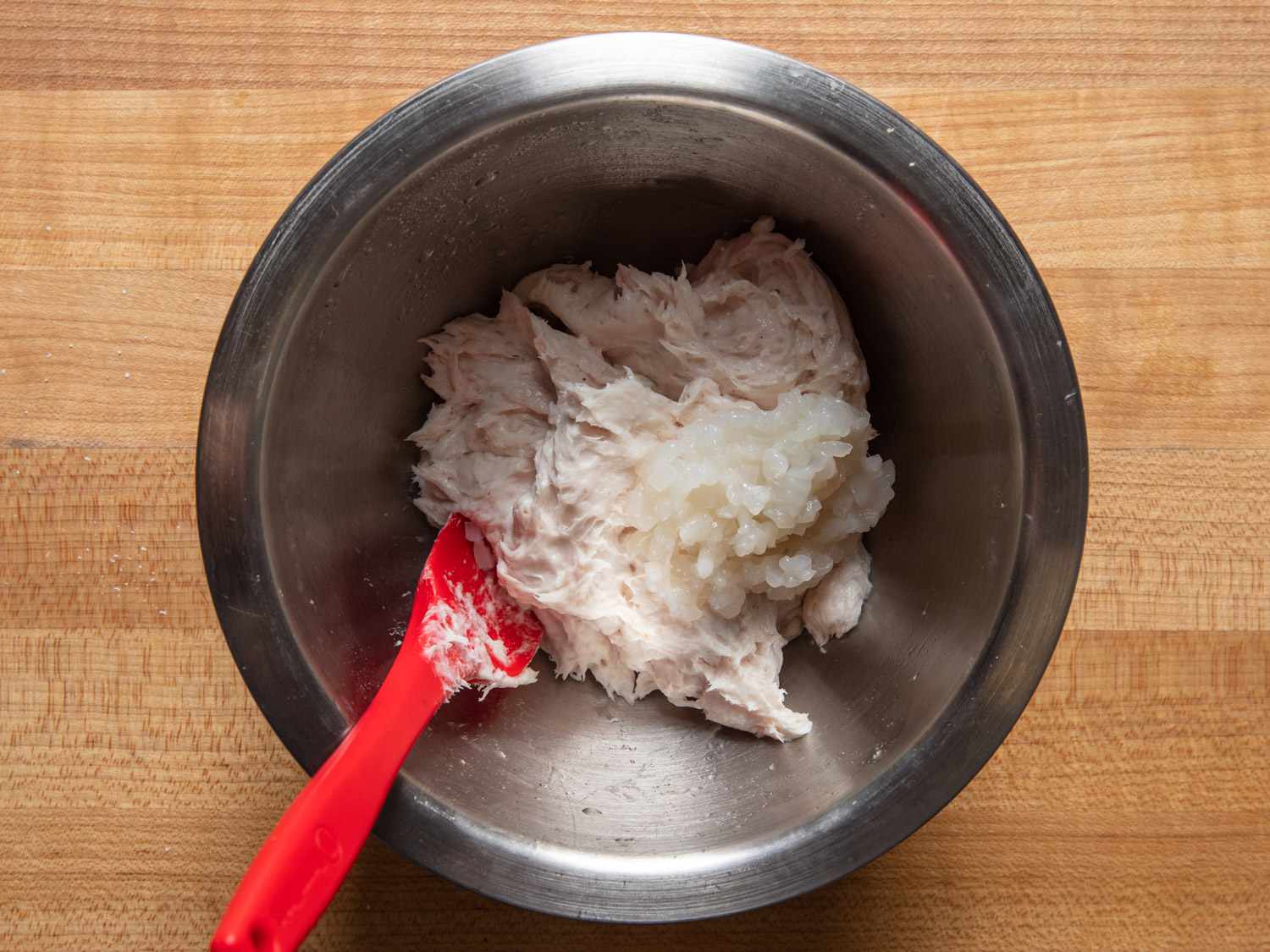 用红色抹刀将加工过的鱿鱼混合物和剁碎的鱿鱼放在碗里的俯视图