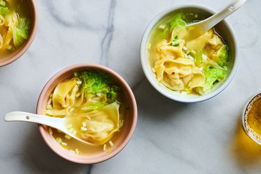 大理石台面上的两碗馄饨汤。每个碗里都有一个白色的陶瓷汤勺。在图像的左上角有另一个碗，右下方的边缘有一杯液体。