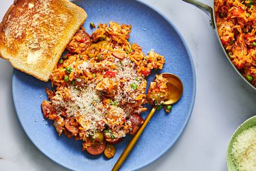 一个蓝色的盘子里盛着一份尼加拉瓜arroz con pollo，还有一片涂了黄油的白面包。盘子上有一把勺子，图像的右侧是一个不锈钢锅，里面装着更多的arroz con pollo，还有一个小碗里装着磨碎的奶酪。