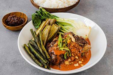 Bowl of kare kare set next to ramekin of shrimp paste and serving bowl of white rice