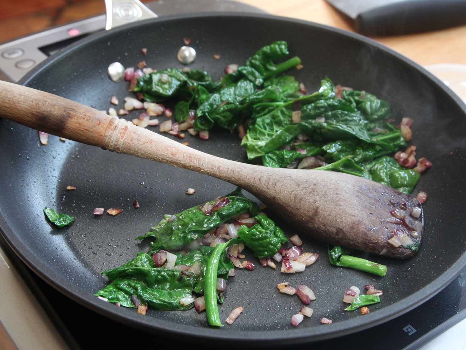 Sautéing菠菜和红洋葱在不粘锅用木勺gydF4y2Ba