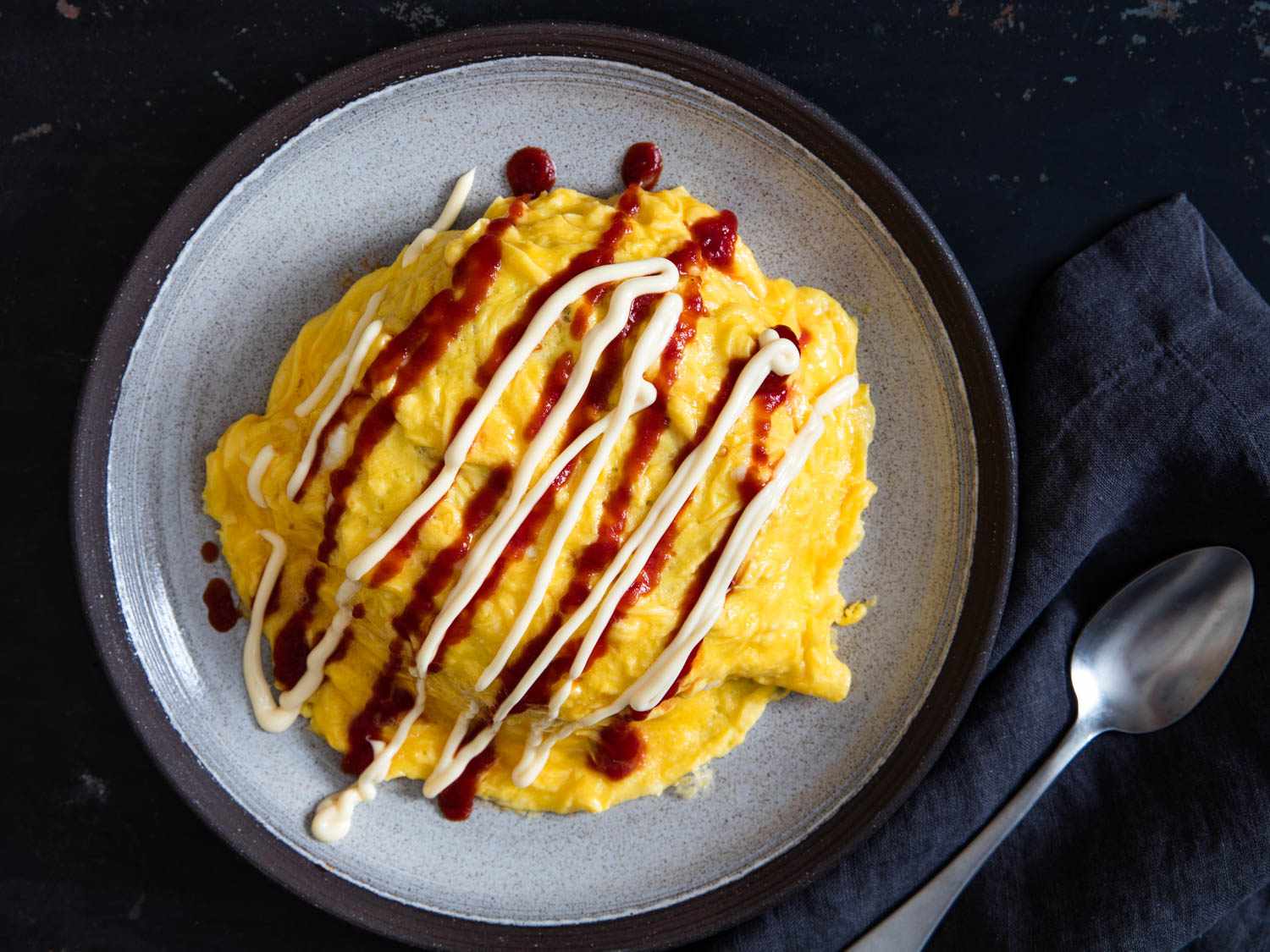 Overhead shot of omurice drizzled with ketchup and Japanese mayo on a plate