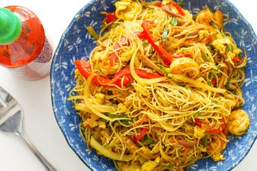 A bowl of curried Singapore rice noodles with char siu, shrimp, bell peppers, and vegetables.