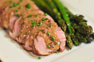 Sliced pork tenderloin topped with a mustard pan sauce and chives, alongside asparagus.