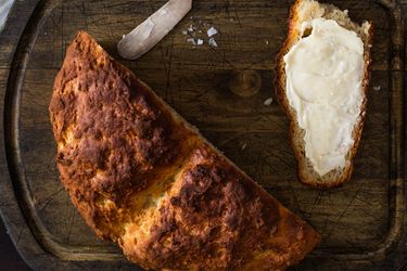 黑木砧板上放着半条爱尔兰苏打面包，旁边放着一片涂了黄油的面包片。