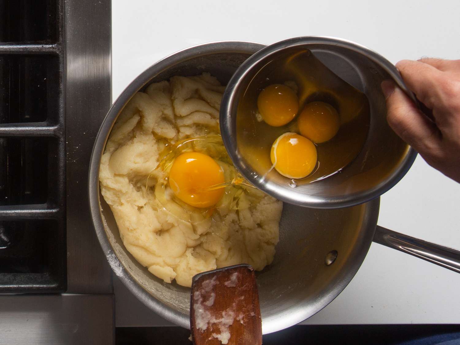 Overhead view of eggs being added to the cooled flour paste, one at a time.