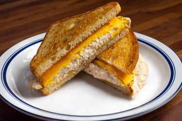 把金枪鱼三明治放在盘子里，对角切成两半，做成三角形;展示了融化的黄色美国奶酪片放在奶油金枪鱼沙拉和烤得很好的面包上。