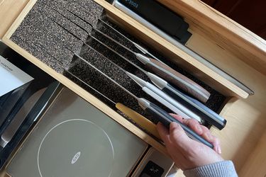 a hand pulling a knife out of a cork-lined drawer insert